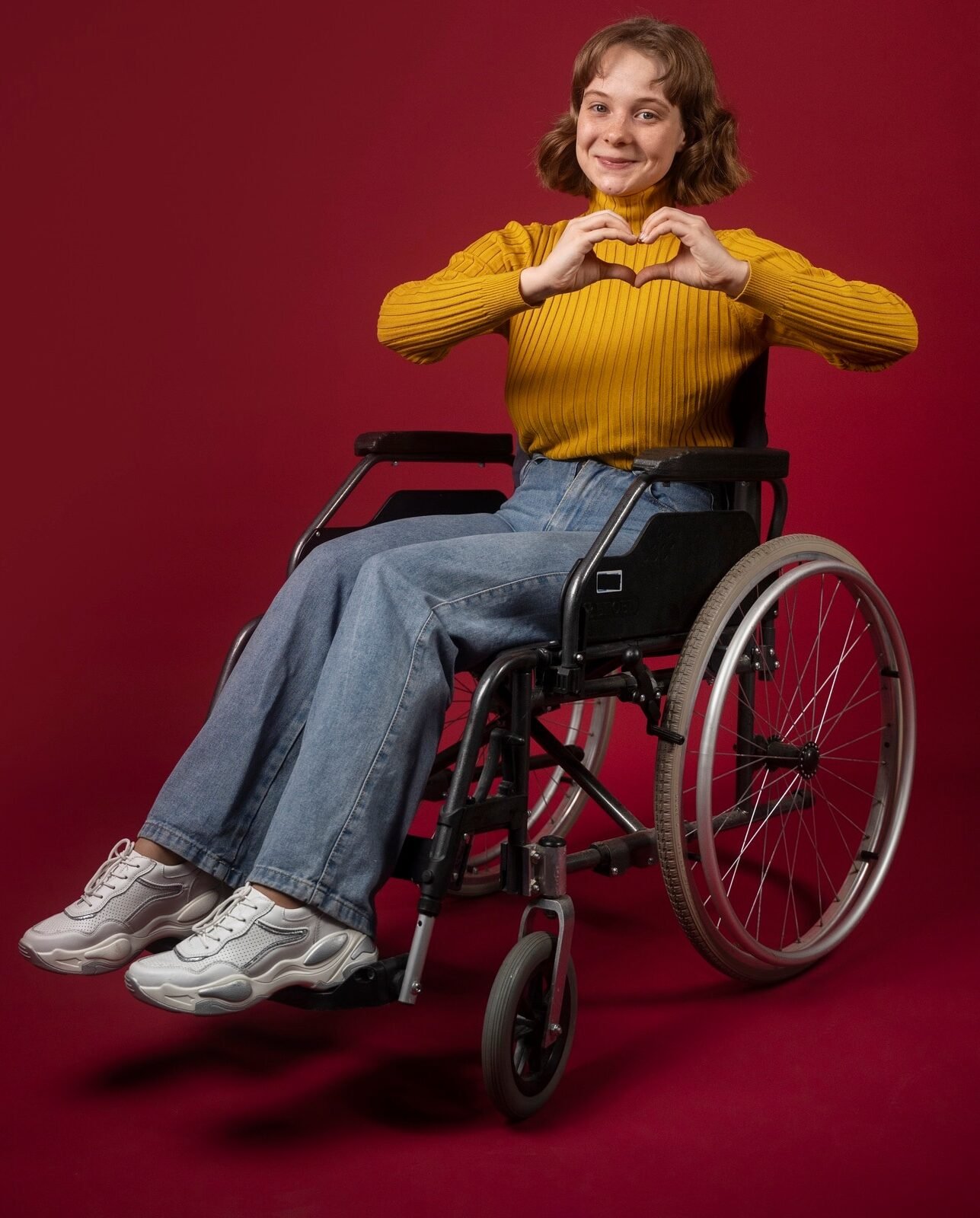 A cute girl on wheelchair making heart with hands